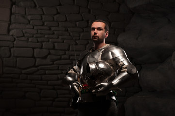 Fototapeta na wymiar Medieval Knight posing with sword in a dark stone background