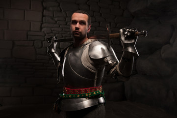 Fototapeta na wymiar Medieval Knight posing with sword in a dark stone background