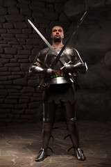 Naklejka premium Medieval Knight posing with two swords on in a dark stone wall b