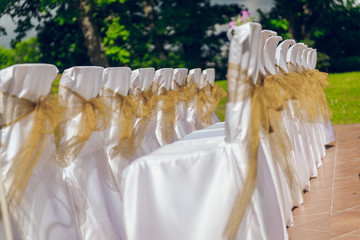 White wedding chairs with brown bows outdoors