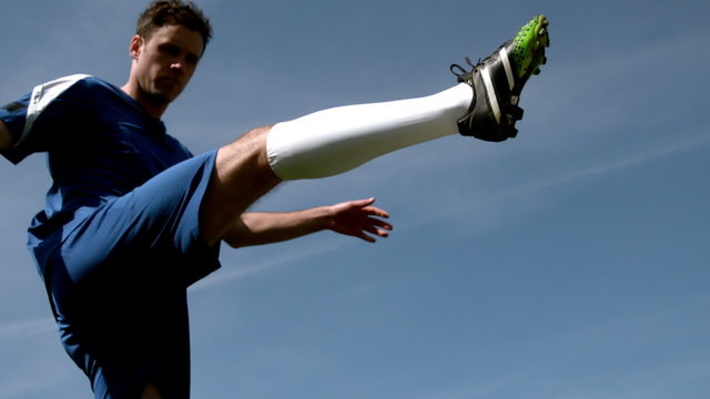 Football player kicking the ball up under blue sky