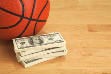 Fototapeta premium Basketball and one hundred dollar bills on wooden court floor