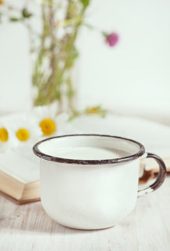 Milk in metal mug and chamomile flowers in open book