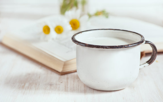 Milk in metal mug and chamomile flowers in open book
