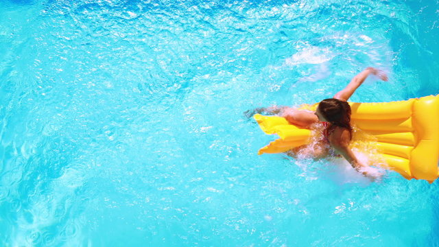 Overhead of brunette sitting on lilo in pool on sunny day