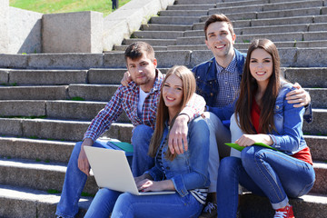 Happy students sitting on stairs in park