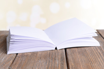 Open white book on wooden table on bright background