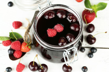 Tasty jam with berries in glass jar on wooden table