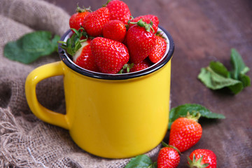 Ripe sweet strawberries in mug  on color wooden background