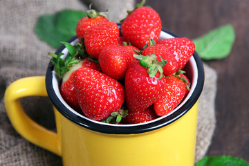 Ripe sweet strawberries in mug  on color wooden background