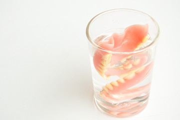 An artificial denture in a glass of water on isolated background