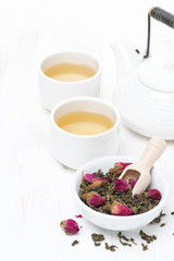 green tea with rosebuds in a bowl, cups and teapot, vertical