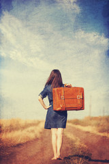 Brunette girl with suitcase on countryside road.