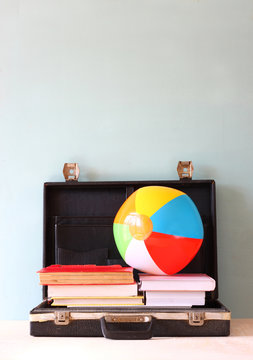 open case with books and beach ball. vacation or travel concept.