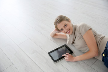 Smiling woman laying on wooden floor with tablet