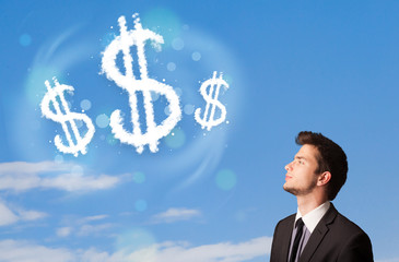 Businesman pointing at dollar sign clouds on blue sky
