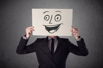 Businessman holding a cardboard with smiley face on it in front