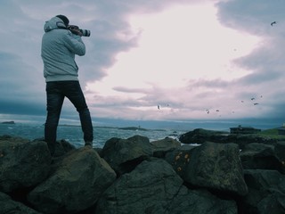 Photographer over rocks shooting seagulls by the sea