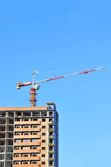 Building crane and building under construction against blue sky