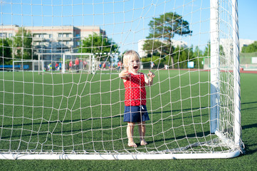 Little girl football fan on the green grass field with ball