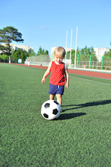 Little girl football fan on the green grass field with ball