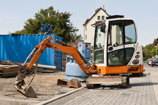 Strassenbau - Ein Minibagger neben einem Baustellentank