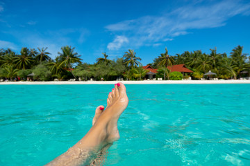 Fototapeta na wymiar Close-up of female foot in the blue water on the tropical beach