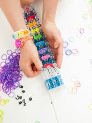 childs hands making a multicoloured elastic band bracelet on a b