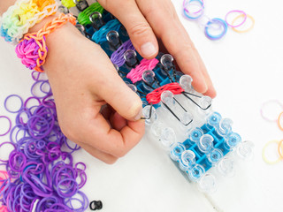 childs hands making a multicoloured elastic band bracelet on a b