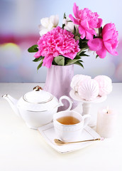 Composition of beautiful peonies in vase, tea in cup and