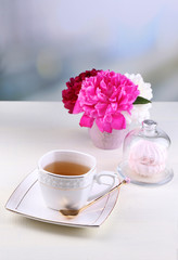 Composition of beautiful peonies in vase, tea in cup and