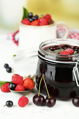 Tasty jam with berries in glass jar on wooden table