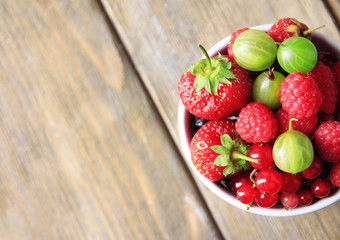 Forest berries in cup, on wooden table background