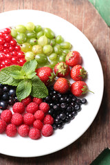 Forest berries on plate, on color wooden background