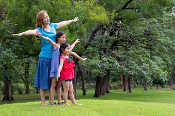 Naklejka na ściany i meble Happy Asian mother and daughter with raised arms in park. Freedom and happiness family concept