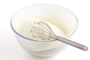 Whisk  in white wheat flour in a glass dish. White background.