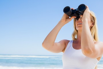 Blonde looking through binoculars on the beach