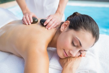 Obraz na płótnie Canvas Happy brunette getting a hot stone massage poolside