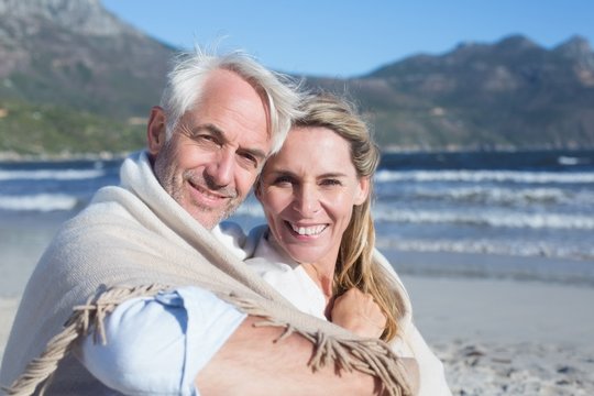 Smiling couple sitting on the beach under blanket