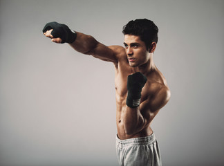 Fit young guy shadowboxing on grey background