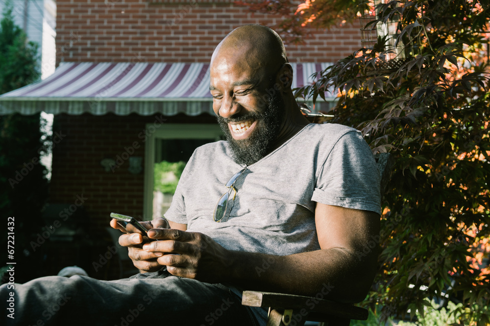 Wall mural man laughs reading text message in garden