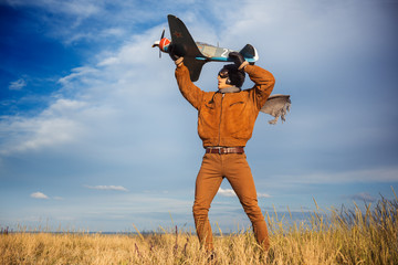 Guy in vintage clothes pilot with an airplane model outdoors