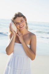 Fototapeta na wymiar Beautiful blonde in white sundress on the beach listening to con
