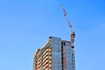 Fototapeta na wymiar Building crane and building under construction against blue sky