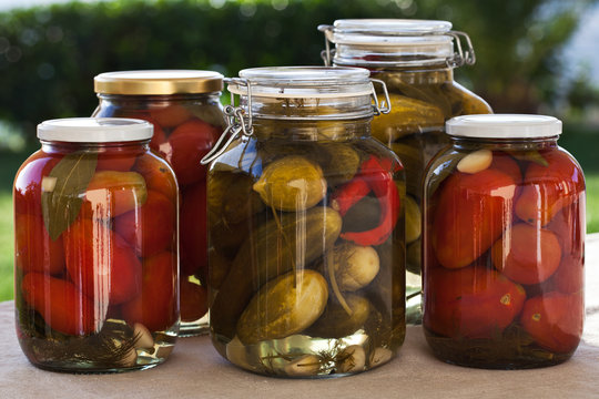 Glass jars of homemade canned tomatoes and cucumbers