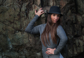 Beautiful young woman in black hat at the rock