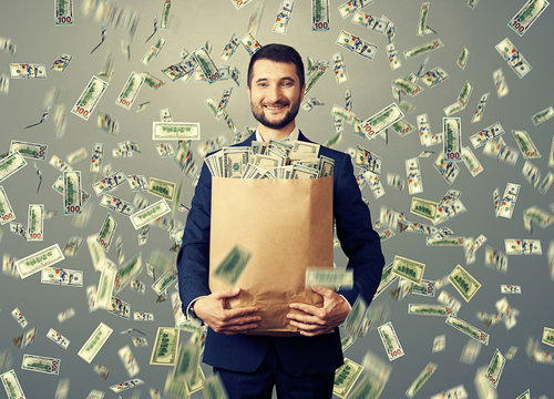 smiley businessman holding paper bag with money