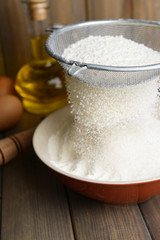 Obraz na płótnie Canvas Sifting flour into bowl on table on wooden background