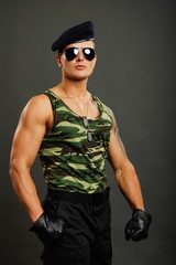 Young military man in leather gloves on gray background