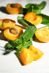 Ripe apricots with green mint leaves on wooden background
